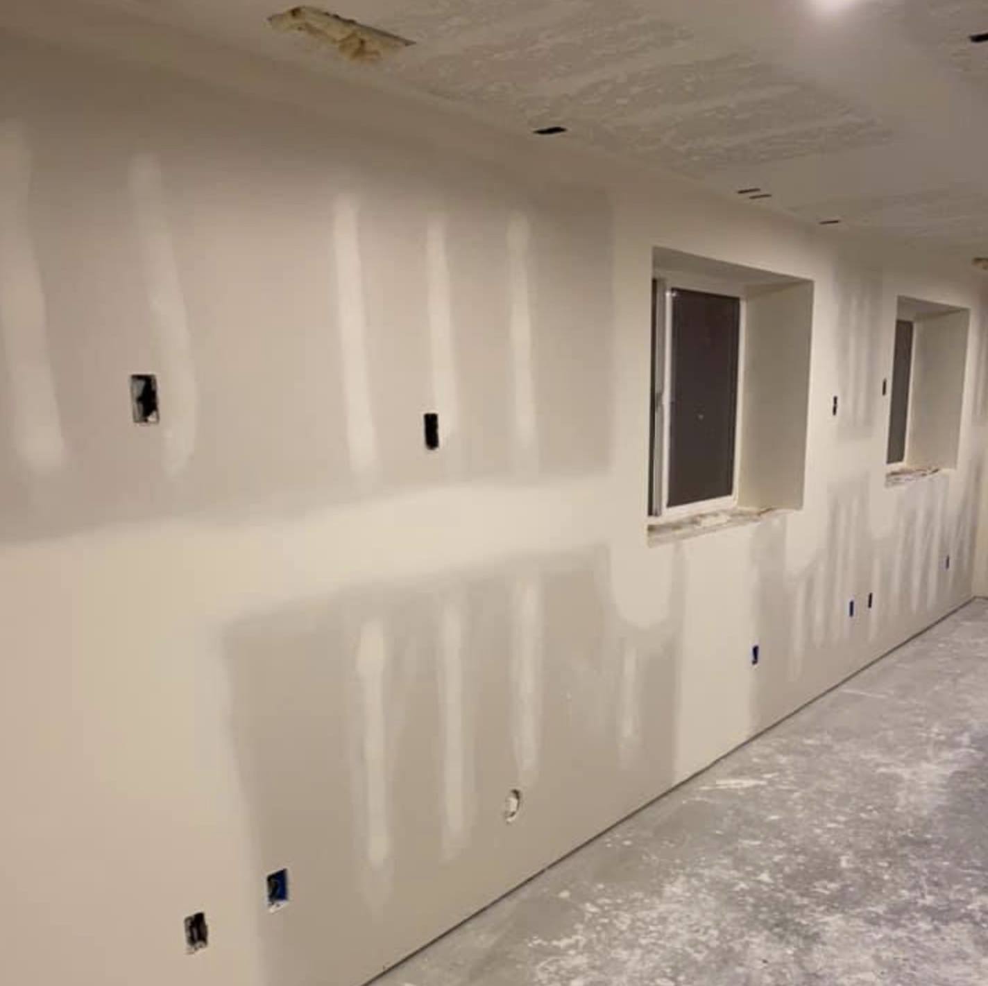 A long basement wall taped, mudded and sanded smooth with window openings framed out