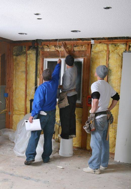 Three EZ Drywall crew members working on a wall with the framing and insulation still exposed