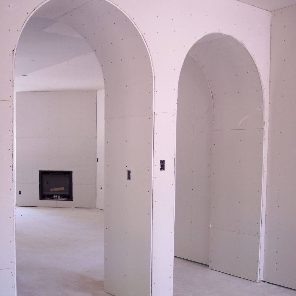 Two finished drywall archways framing a living room with a fireplace beyond